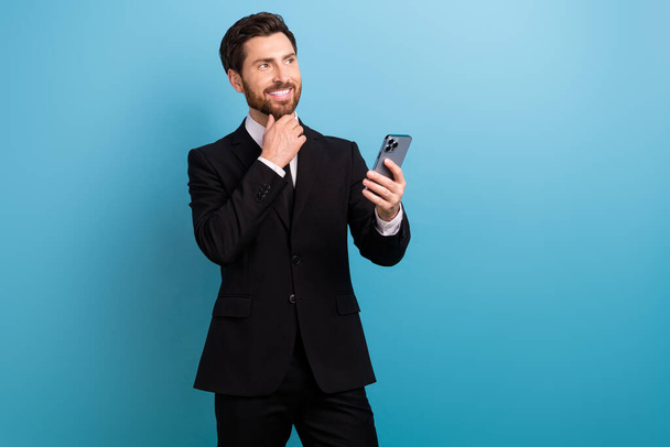 Photo of happy thoughtful advisor wear black tuxedo chatting modern gadget looking empty space isolated blue color background. - Foto, imagen
