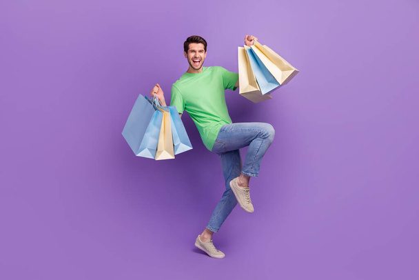 Full length photo of young shopaholic guy hands hold shopping bags advertisement celebrate black friday offer isolated on purple background. - 写真・画像