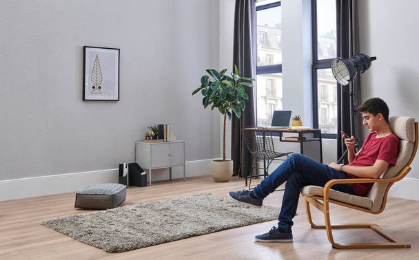 Mladý a dospívající muž v moderním pojetí pokoje, židle, zeď, výzdoba interiéru. - Fotografie, Obrázek