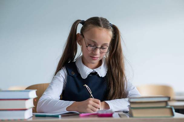 Caucasian girl with two ponytails sits at her desk and writes in a workbook - Foto, immagini