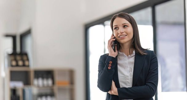 Krásná mladá usměvavá obchodní žena volat přes smartphone při práci na dálku z kanceláře. - Fotografie, Obrázek
