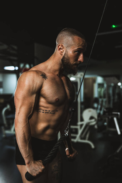 Ein junger muskulöser Bodybuilder, der im Fitnessstudio hart für seine Armmuskeln trainiert. - Foto, Bild