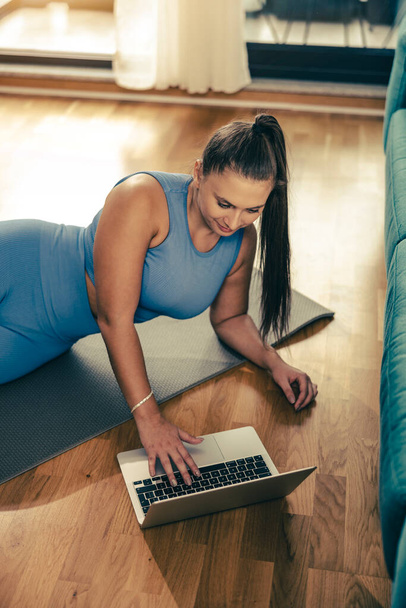 Junge Frau benutzt Laptop beim Fitnesstraining zu Hause am Morgen. - Foto, Bild