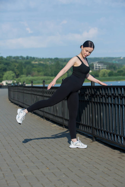 Portret uśmiechniętej młodej kobiety w czarnej odzieży sportowej ćwiczącej na świeżym powietrzu. Koncepcja sprawności i zdrowego stylu życia. - Zdjęcie, obraz