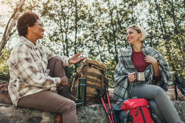 二人のレースの女性の友人は、森の中で彼らのハイキングを通して茶休憩を取ります. - 写真・画像