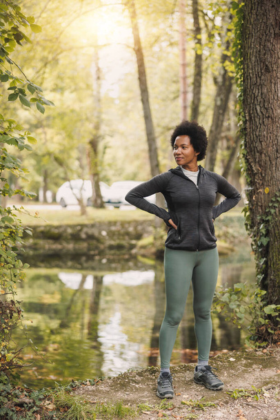 Linda maduro afro-americano feminino corredor relaxante após treinamento esportivo na manhã perto do rio na natureza. - Foto, Imagem