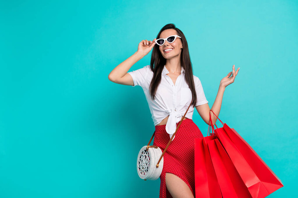 Photo of funky pretty lady dressed white crop top purse dark eyewear holding red shoppers empty space isolated turquoise color background. - Fotografie, Obrázek