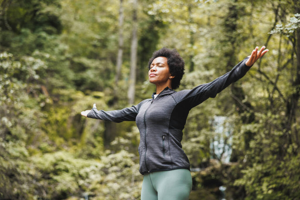 Czarna kobieta stojąca w naturze z wyciągniętymi ramionami i ciesząca się świeżym powietrzem. - Zdjęcie, obraz