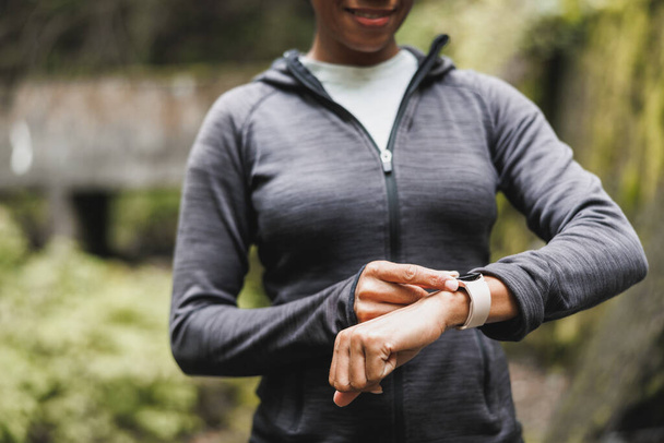 Close-up of a unrecognizable black female person looking at smartwatch and preparing to do jogging in the nature. - 写真・画像