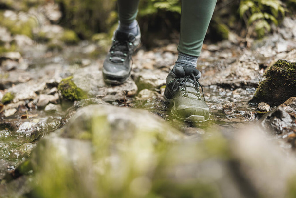Foto ritagliata di una donna escursionista irriconoscibile che attraversa un ruscello mentre esplora nel bosco. - Foto, immagini