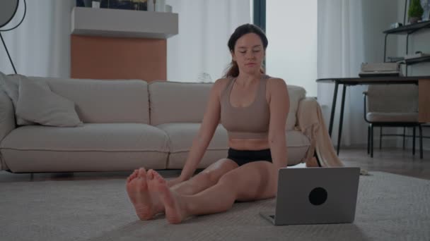 брюнетка с помощью ноутбука смотреть онлайн класс йоги тренировки поезда на дому женщина в спортивной одежде - Кадры, видео