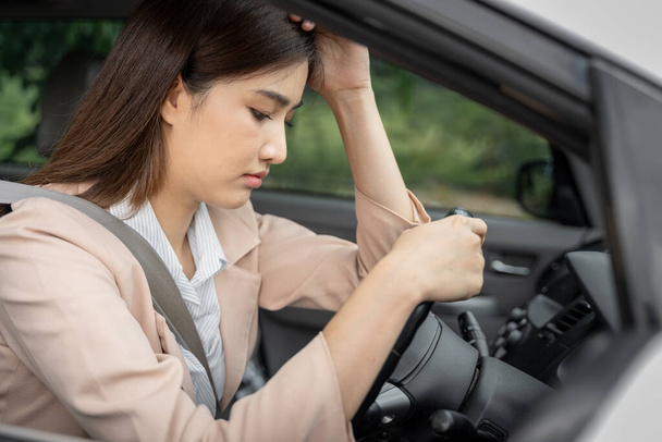 Грустная и уставшая молодая азиатская офисная работница, сидящая в машине, думает о своих проблемах на работе - Фото, изображение