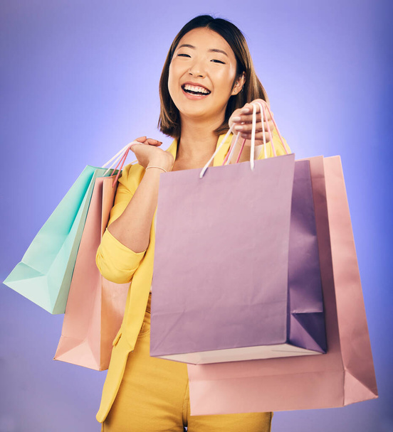Shopping bag, portrait and woman giving, offer or fashion discount, deal or sale on studio purple background. Giveaway, prize or competition of young customer, model or asian person winning in retail. - Photo, Image