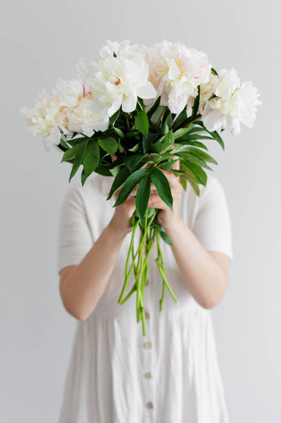 Young woman in dress hiding face behind peony bouquet - Zdjęcie, obraz