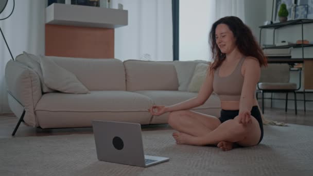 vrouw dragen sport kleding zitten op de vloer online klasse met yoga trainer glimlachen brunette kijken op display laptop doen oefening - Video