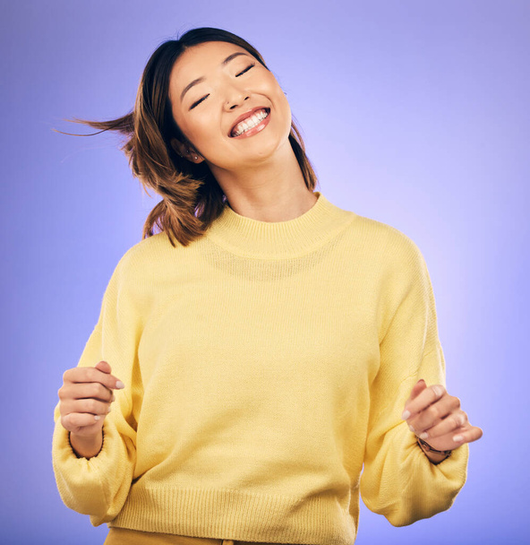 Happy asian woman, dancing and enjoying music, freedom or casual fashion against a purple studio background. Female person or model smile for energy, event or party in happiness for clothing style. - Photo, Image