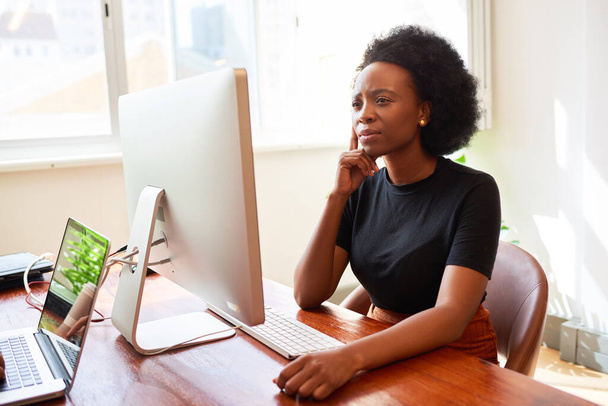 Młoda, czarna bizneswoman rozmawia przez telefon w jasnym biurze, uruchamia technologię. Wysokiej jakości zdjęcie - Zdjęcie, obraz