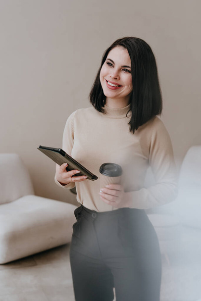 Young brunette businesswoman using a tablet against a light wall indoor. Selective focus. - Foto, Imagem