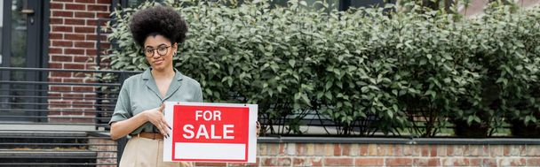положительный африканский американский брокер недвижимости стоять с для продажи вывеска рядом со зданием, баннер - Фото, изображение