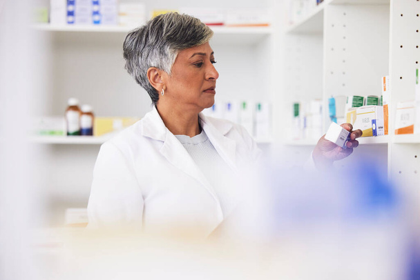 Pharmacist, shelf and a woman reading a medicine box label in a pharmacy for knowledge. Mature female employee in healthcare, pharmaceutical and medical industry to check product information on stock. - 写真・画像