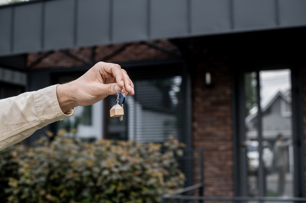 Teilansicht eines professionellen Immobilienmaklers mit Schlüssel in der Nähe moderner Hütte auf verschwommenem Hintergrund - Foto, Bild