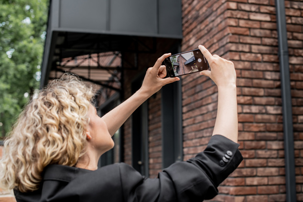 blondi kiinteistönvälittäjä matkapuhelimella ottaa valokuvan modernin talon kaupungin kadulla - Valokuva, kuva