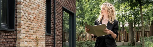 atrakcyjny blond agent nieruchomości z folderu patrząc na budynek na ulicy miejskiej, baner - Zdjęcie, obraz