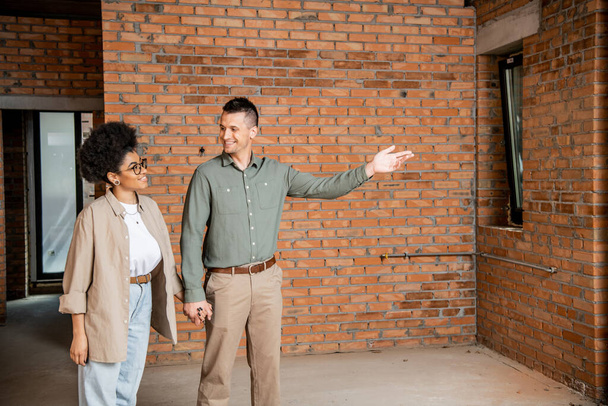 happy man pointing with hand while showing new house to african american woman - Photo, Image