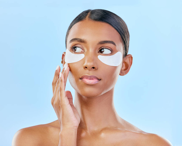 Face, eye patch and beauty of a woman with natural skin glow on a blue background. Dermatology, collagen mask and cosmetics of Indian female model for facial shine, wellness or self care in studio. - Photo, Image