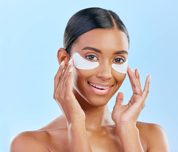 Happy, skincare and portrait of woman with patches for eyes, dark circles and treatment. Smile, face and Indian girl or model with a facial collagen for a glow isolated on a blue background in studio. - Photo, Image