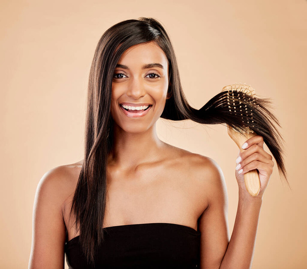 Portrait, beauty and a woman brushing her hair in studio on a cream background for natural or luxury style. Haircare, face and shampoo with a young indian female model at the salon or hairdresser. - Foto, afbeelding