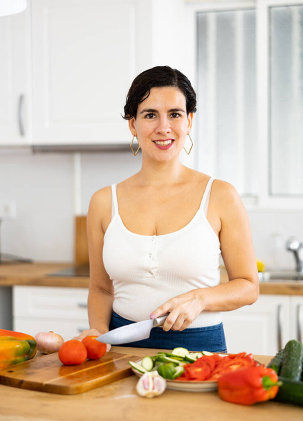 Vidám fiatal spanyol nő egészséges étrendet követve zöldségsalátát készít vacsorára az otthoni konyhában - Fotó, kép
