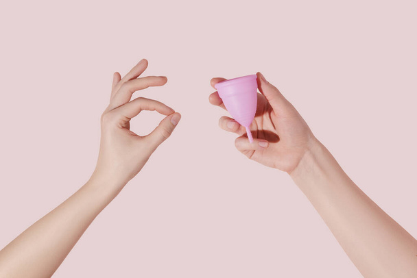 Mão feminina com copo menstrual reutilizável em fundo rosa. Mão feminina fazendo sinal ok - Foto, Imagem