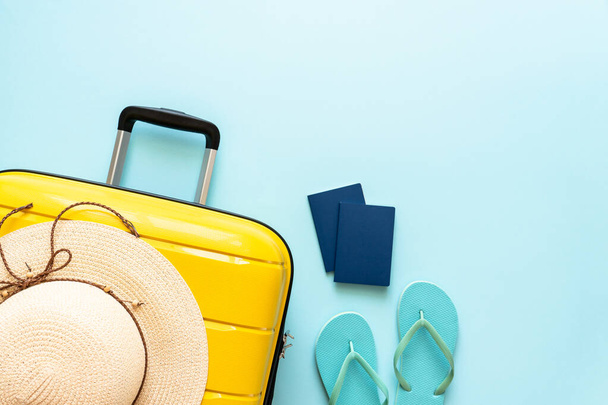 Βαλίτσα, καπέλο, διαβατήρια και σαγιονάρες σε μπλε φόντο. Καλές γιορτές, ταξιδιωτική ιδέα. Επίπεδη εικόνα. - Φωτογραφία, εικόνα