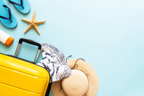 Suitcase, hat and flip flops on blue background. Happy Holidays, travel concept. Flat lay image. - Photo, Image
