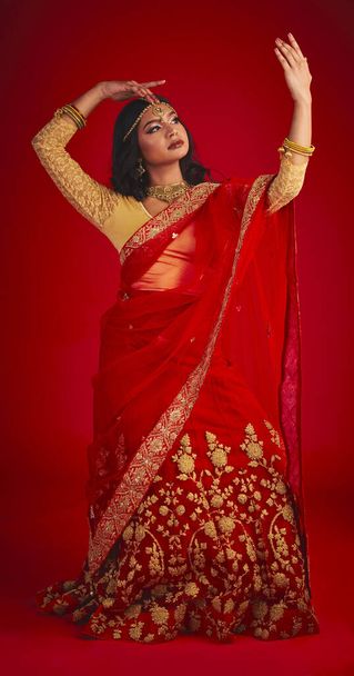 Beauty. dance and Indian woman in a traditional dress, jewellery and religion against a red studio background. Female person, girl and dancer with a cultural outfit, dancing and routine with fashion. - Valokuva, kuva