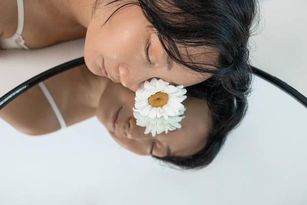 Detailní záběr krásná svěží tvář s květinovou sedmikráskou a kapkami vody na kůži. Krásný asijský model se zrcadlem. - Fotografie, Obrázek