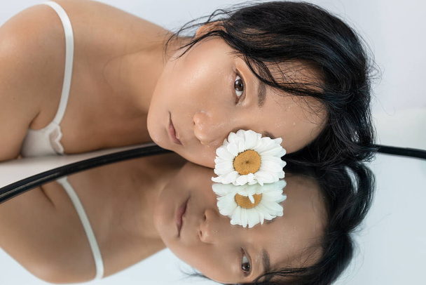 Close-up belo rosto fresco com flor de margarida e gotas de água na pele. Beleza modelo asiático com espelho. - Foto, Imagem