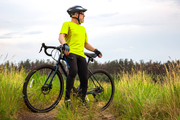 Sarı elbiseli sakallı bisikletçi doğada bir bisikletin üzerinde dinleniyor. Spor, hobiler ve sağlık için eğlence - Fotoğraf, Görsel