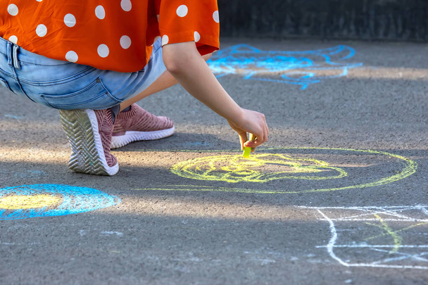 Дівчина малює усміхнене обличчя з жовтим крейдою на тротуарі. Творчість та захоплення дітей розваги та відпочинку - Фото, зображення