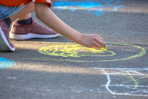 Дівчина малює усміхнене обличчя з жовтим крейдою на тротуарі. Творчість та захоплення дітей розваги та відпочинку - Фото, зображення