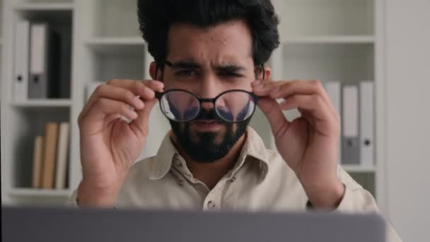 niezdrowy indyjski arabski człowiek w okularach dla laptop biznes praca mylić biznesmen biuro dyrektor generalny z zły wzrok niewyraźne oczy krótkowzroczność zdjąć okulary medyczne oko laserowa korekcja wzroku - Materiał filmowy, wideo