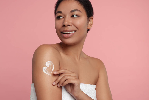 Young woman applying body cream onto arm on pink background - Fotoğraf, Görsel