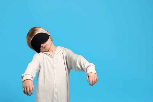 Boy in pajamas and sleep mask sleepwalking on light blue background, space for text - Фото, зображення