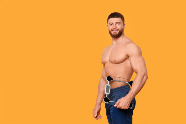 Portrait of happy athletic man with scales on orange background, space for text. Weight loss concept - Foto, imagen