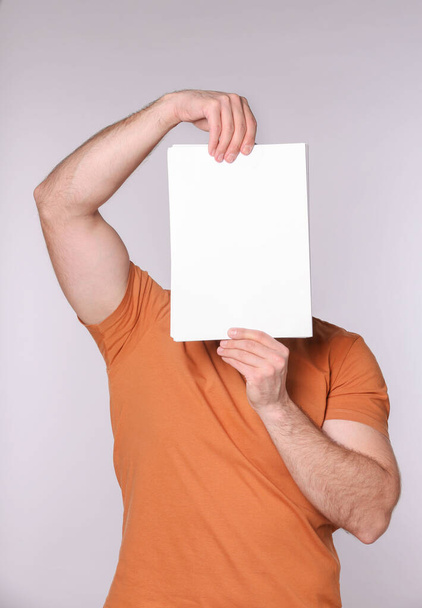 Man covering face with sheet of paper on light grey background. Mockup for design - Фото, зображення