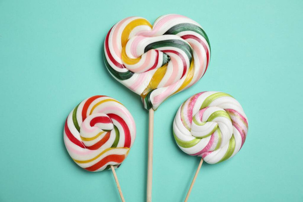 Sticks with different colorful lollipops on turquoise background, flat lay - Zdjęcie, obraz