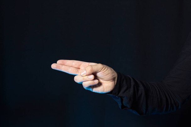 Een man die zijn hand gebruikt om twee vingers te wijzen voor een donkere achtergrond. Afbeelding met kopieerruimte. - Foto, afbeelding