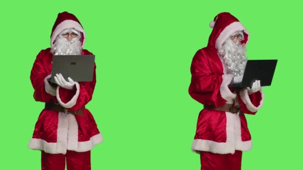 Man in santa costume using laptop to see naughty or nice children list, looking around the globe to send presents on christmas eve. Father christmas concept, person on greenscreen. - Footage, Video