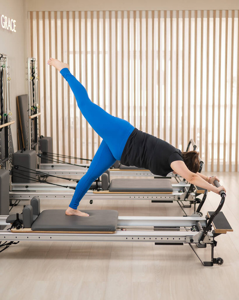 Overweight caucasian woman doing pilates exercises on a reformer - Foto, immagini